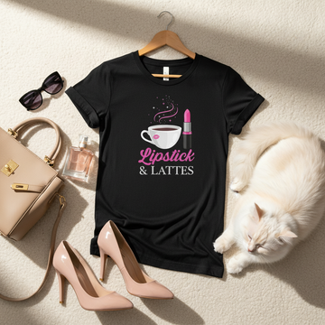 Black t-shirt with 'Lipstick & Lattes' design on a hanger, surrounded by high heels, handbag, sunglasses, and a cat.